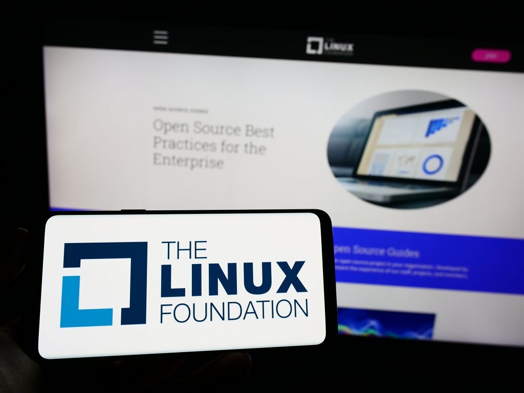 Image showcasing The Linux Foundation logo on a smartphone screen, with a blurred background featuring a website about "Open Source Best Practices for the Enterprise." The image highlights the prominence of The Linux Foundation in promoting open-source software and best practices in enterprise environments.