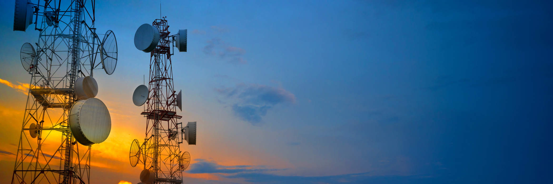 Telecommunications towers against a sunset. Edge computing allows for 5G network performance via edge devices like telecom towers.