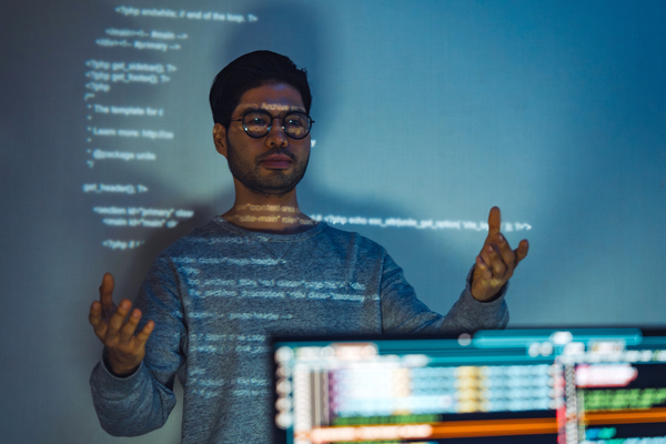 A man, assisted by AI-powered operations, views code projected from computer