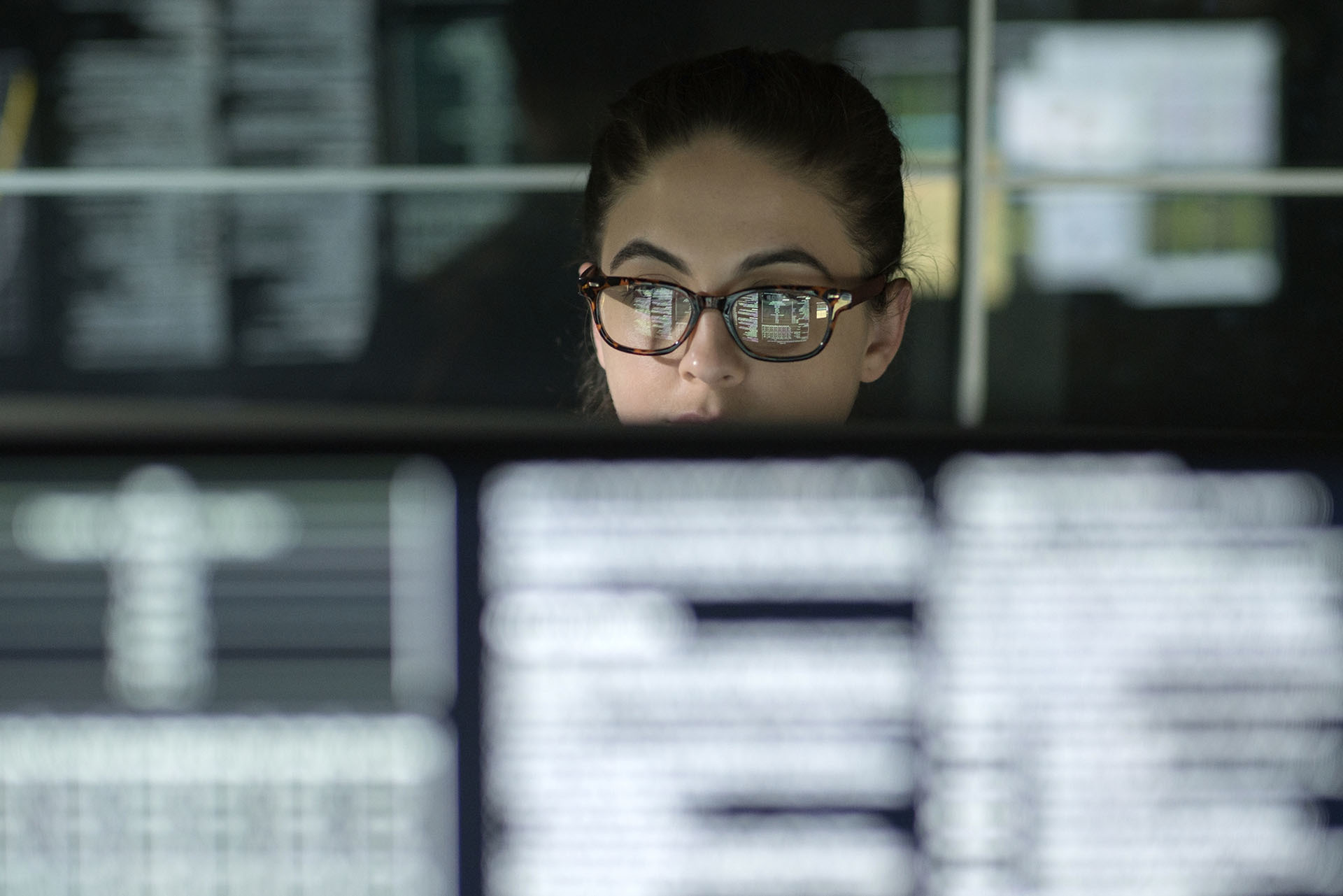 A woman, assisted by AI-powered operations, reviews data on computer monitors