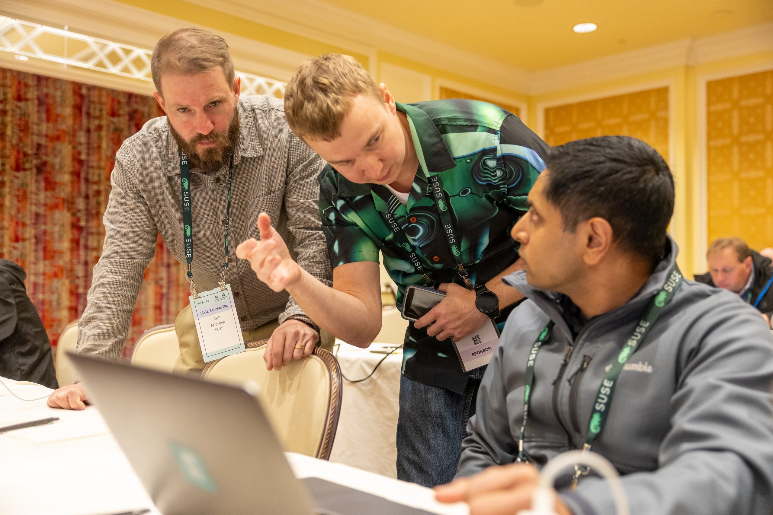 Three attendees at SUSE Rancher Day 2024 look at a computer, where they are testing out SUSE Rancher Prime with Virtualization