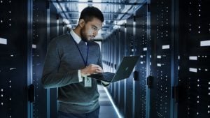 Man holding laptop in front of servers