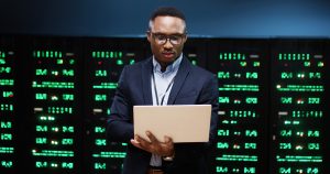 Man holding laptop in front of computer servers